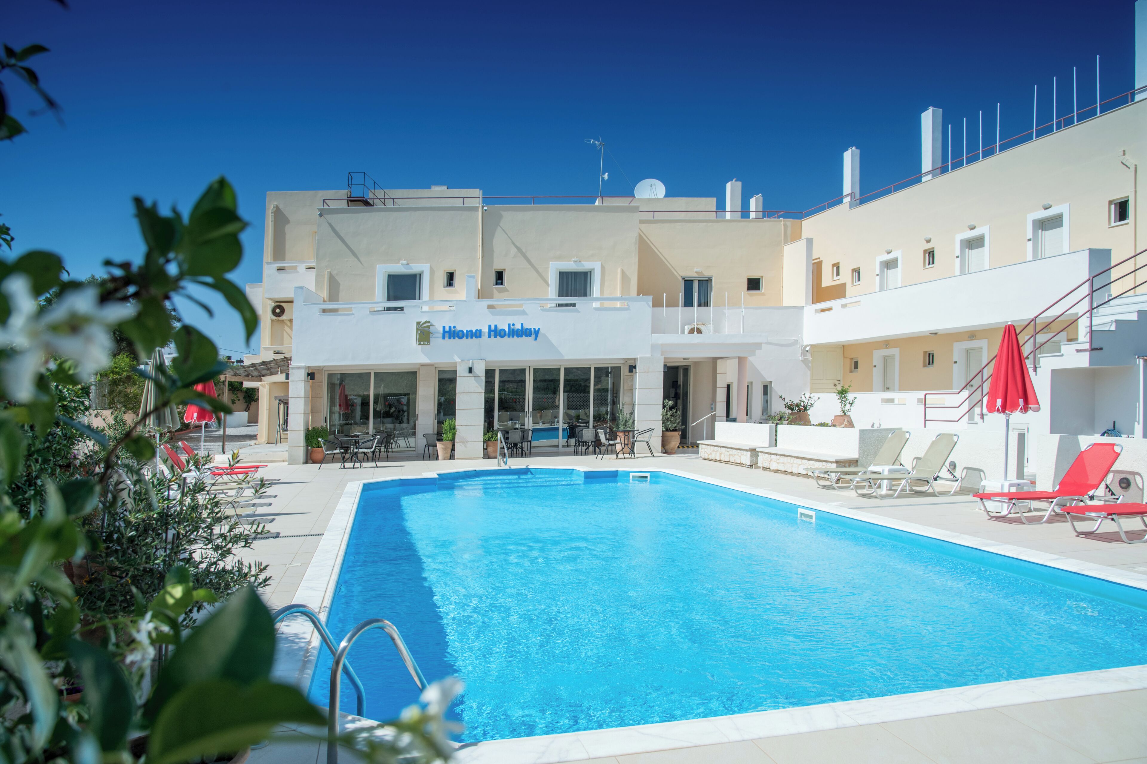 A hotel with a swimming pool, outdoor seating, and a clear blue sky.