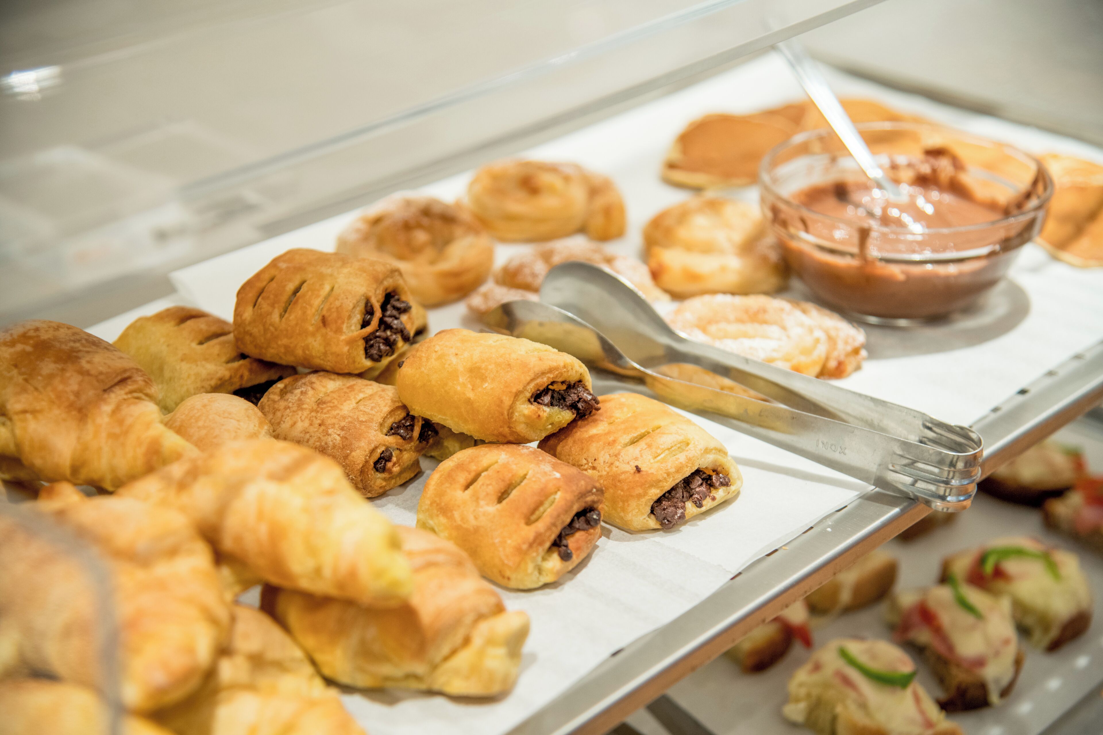 Exposição de vários doces e uma tigela de creme de chocolate numa pastelaria.