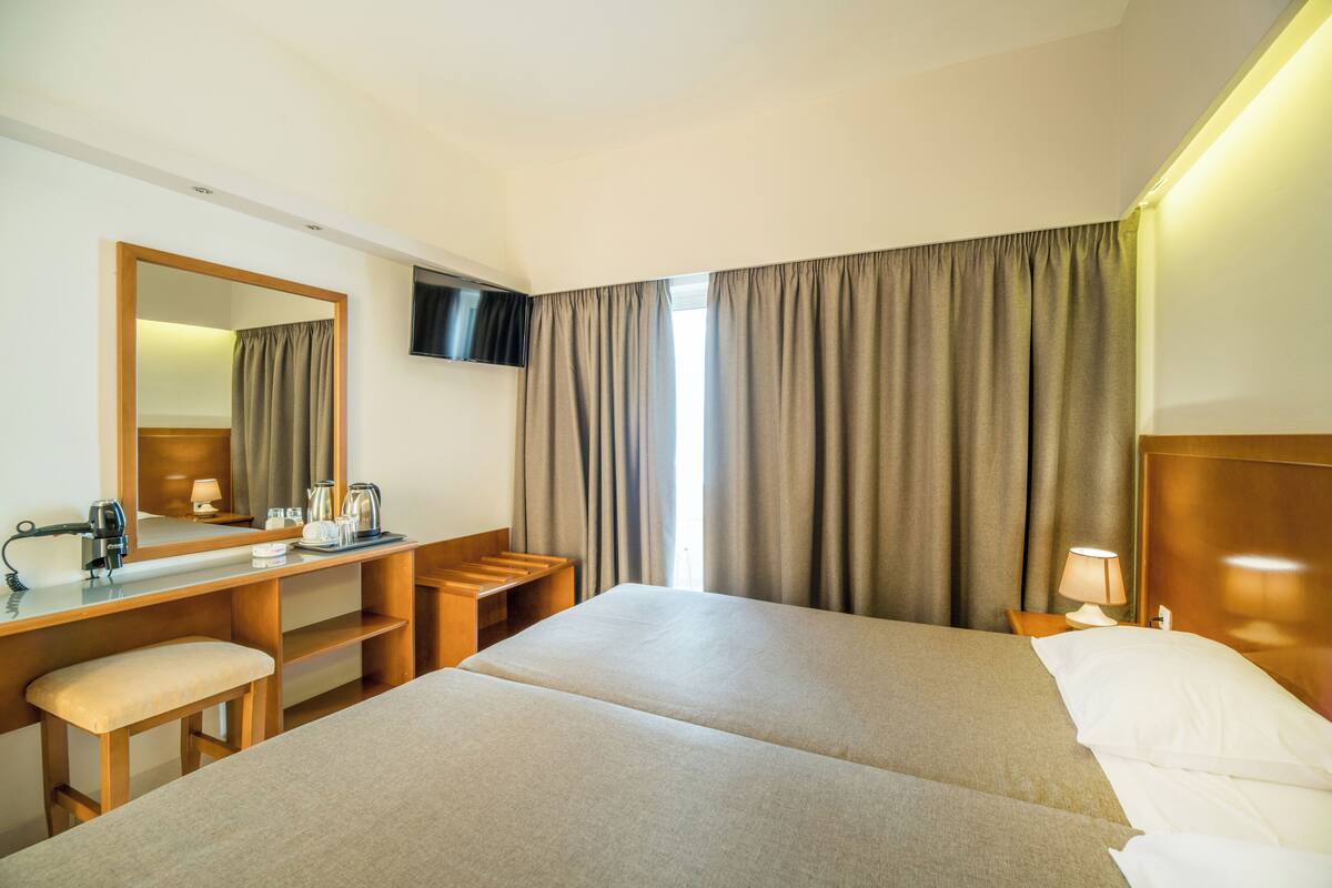 A hotel room with a bed, a desk with a chair, a TV, and a window with curtains.