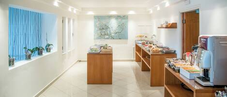 A modern hotel lobby with a reception desk, a coffee machine, and a large window with plants.
