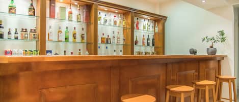 A bar area with wooden stools and shelves stocked with various bottles.