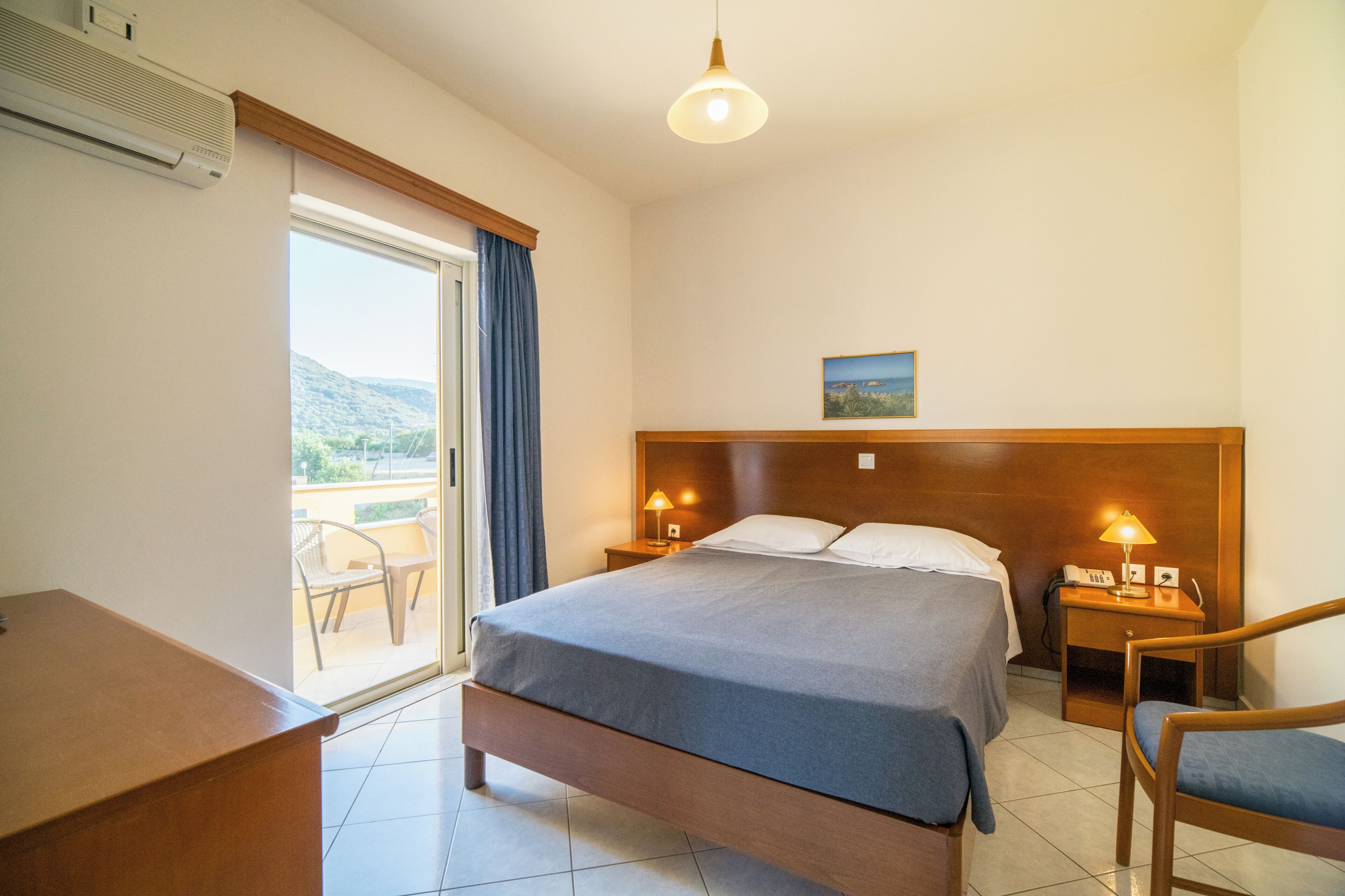 Une chambre d’hôtel avec un grand lit, deux tables de chevet avec des lampes, une tête de lit en bois, une vue sur l’extérieur et un bureau.