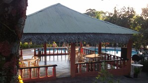 Un área junto a la piscina con un espacio de estar techado, una piscina y una estructura de techo de paja.