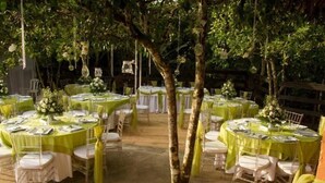 Un espacio para eventos al aire libre con mesas redondas cubiertas con manteles verdes, sillas blancas y centros de mesa florales.