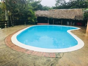 A swimming pool with a thatched roof structure in the background. - Los Bohios Campo Añil (Jarabacoa)