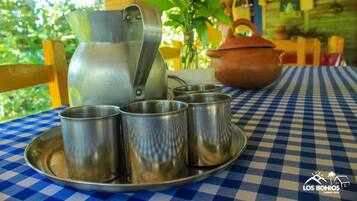 A metal pitcher, four metal cups, and a clay pot on a checkered tablecloth.