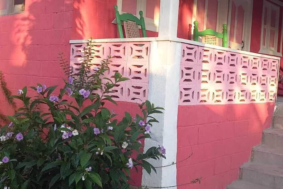 Un bâtiment rouge avec des encadrements de fenêtres blancs, une chaise verte et une clôture blanche décorative.
