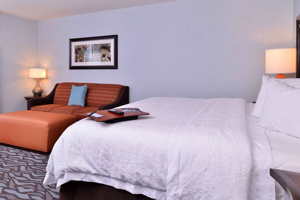 A hotel room with a large bed, a sofa, a desk with a lamp, and a framed picture on the wall.