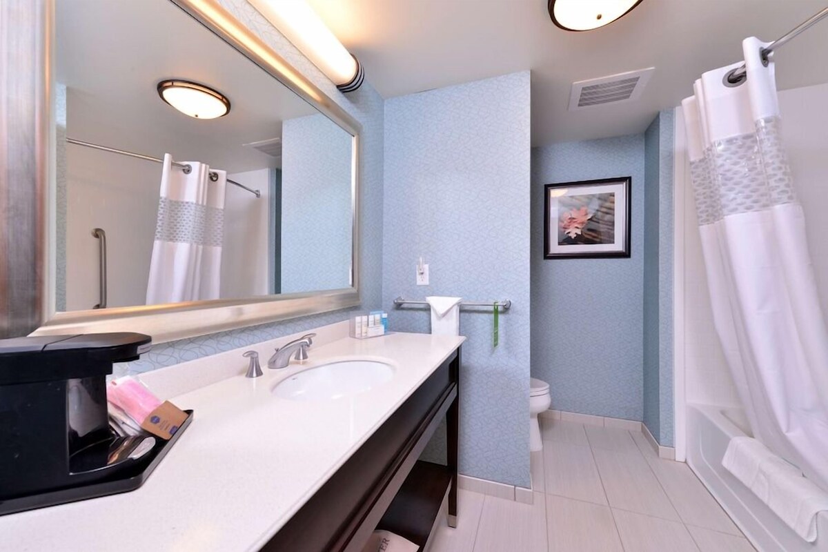 A modern bathroom with a large mirror, two sinks, a toilet, and a shower area.
