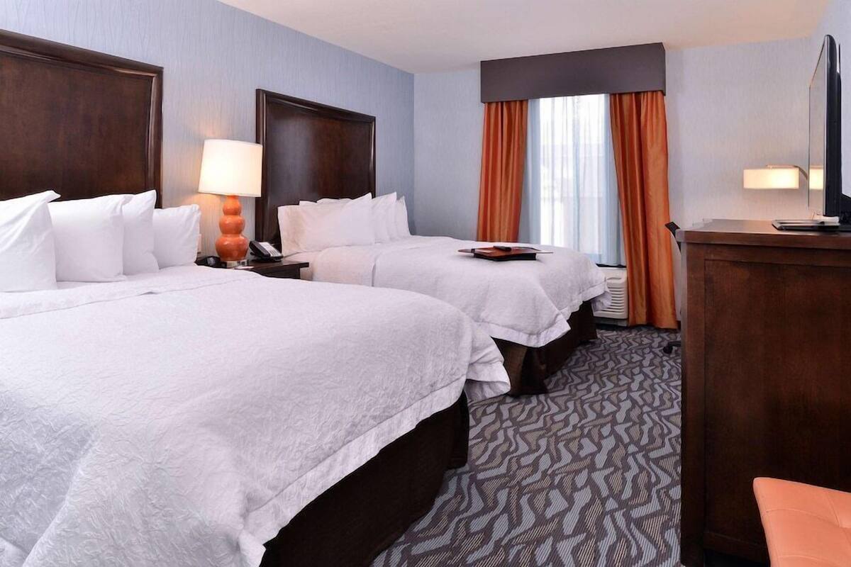 A hotel room with two beds, a desk, a television, and a window with curtains.
