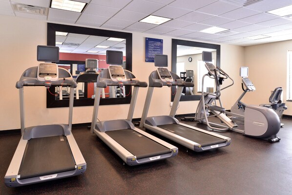 Four treadmills in a gym with control panels, a mirrored wall, and a clock.