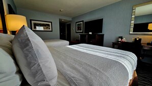 A hotel room with a large bed, a desk, a chair, a TV, and a lamp.