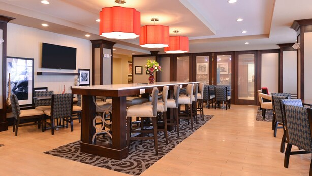 A spacious lobby with a long reception desk, multiple seating areas, and a large flat-screen TV mounted on the wall.