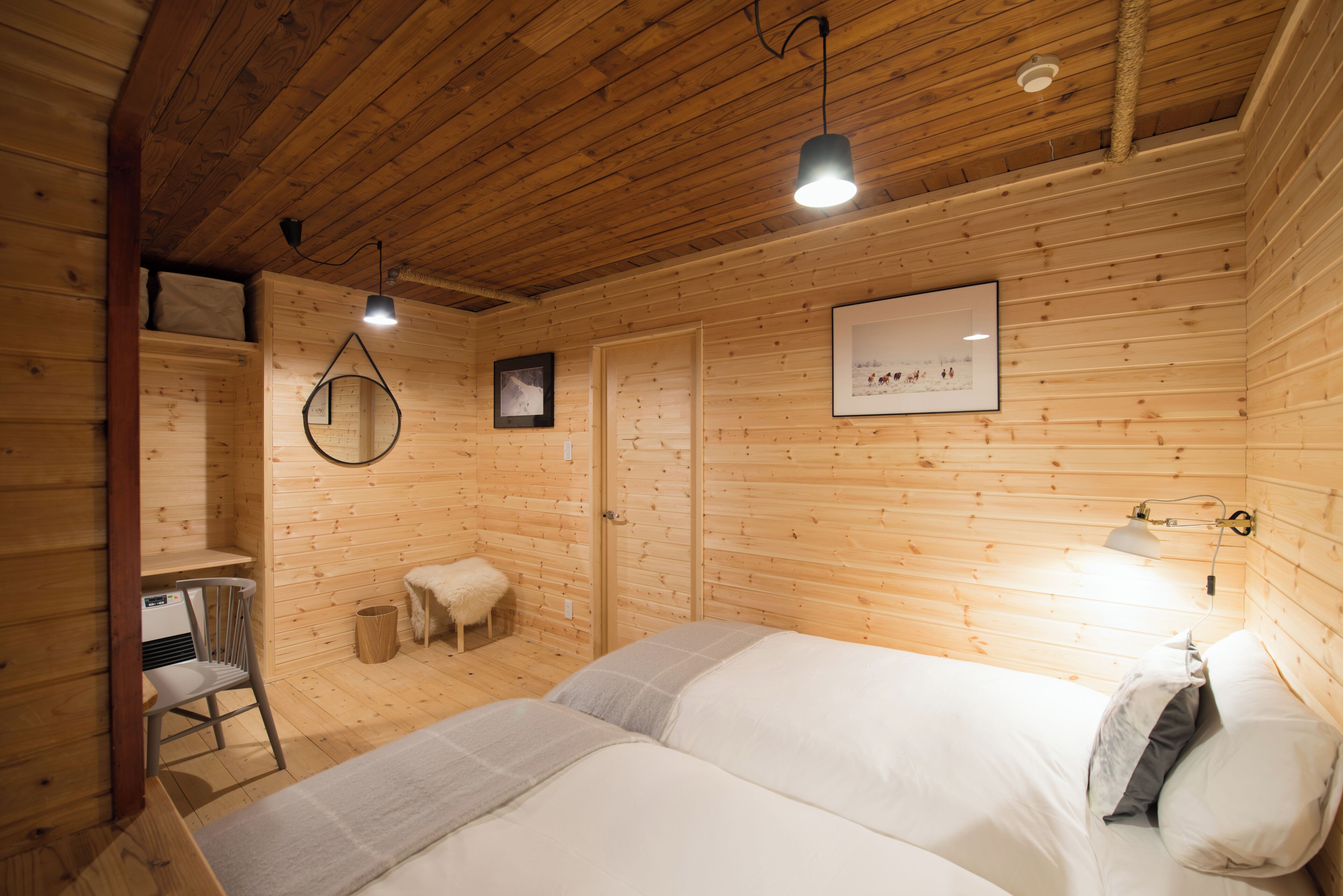 A wooden cabin bedroom with two beds, a chair, a small stool, and a framed picture on the wall.