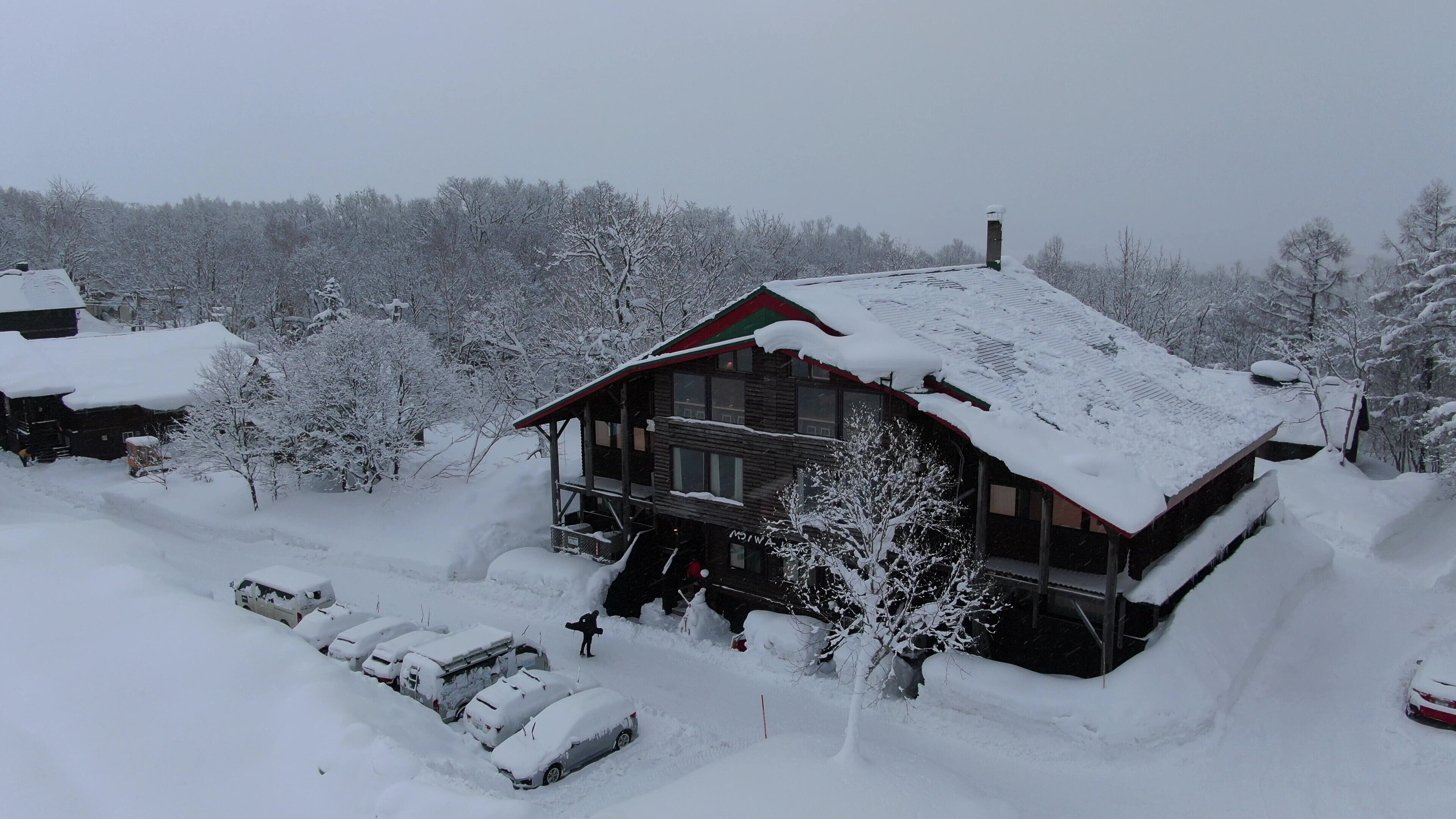 A snow-covered lodge with a wooden exterior, a red roof, and a visible entrance.