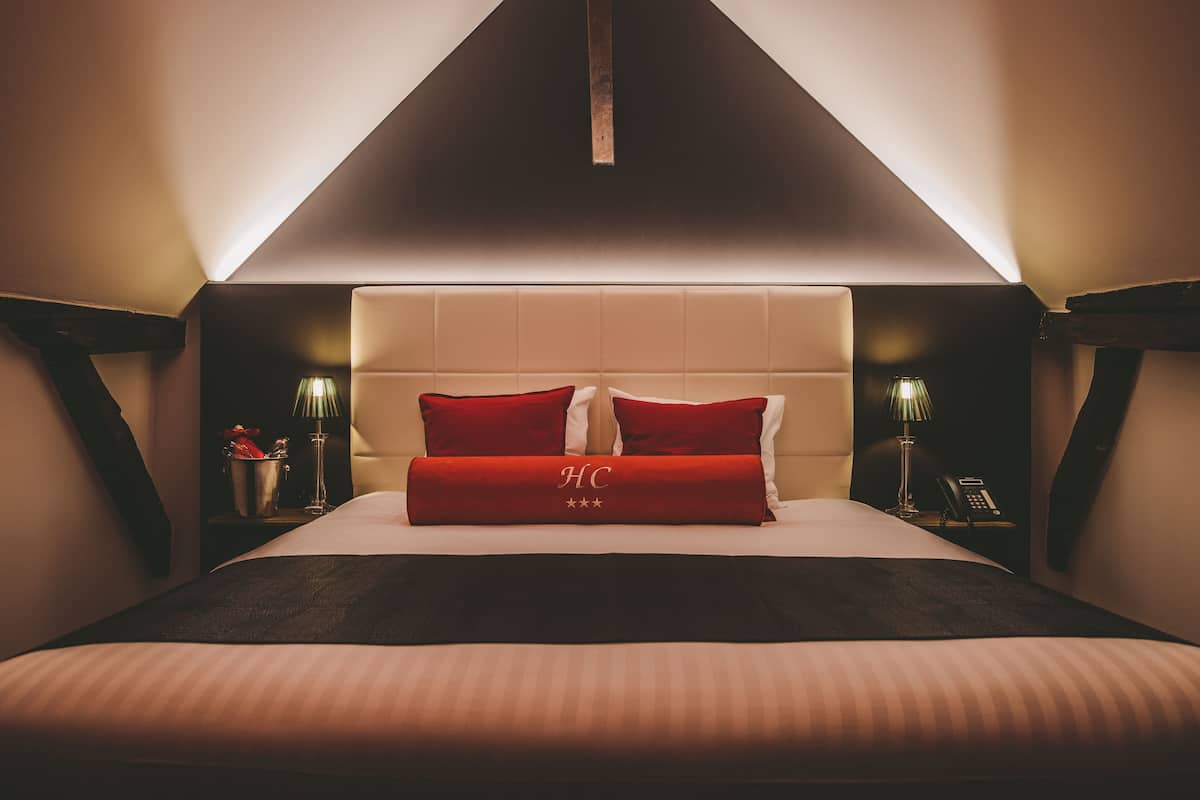 A hotel room with a large bed, a headboard with a light fixture, bedside tables with lamps, and a nightstand with a telephone.