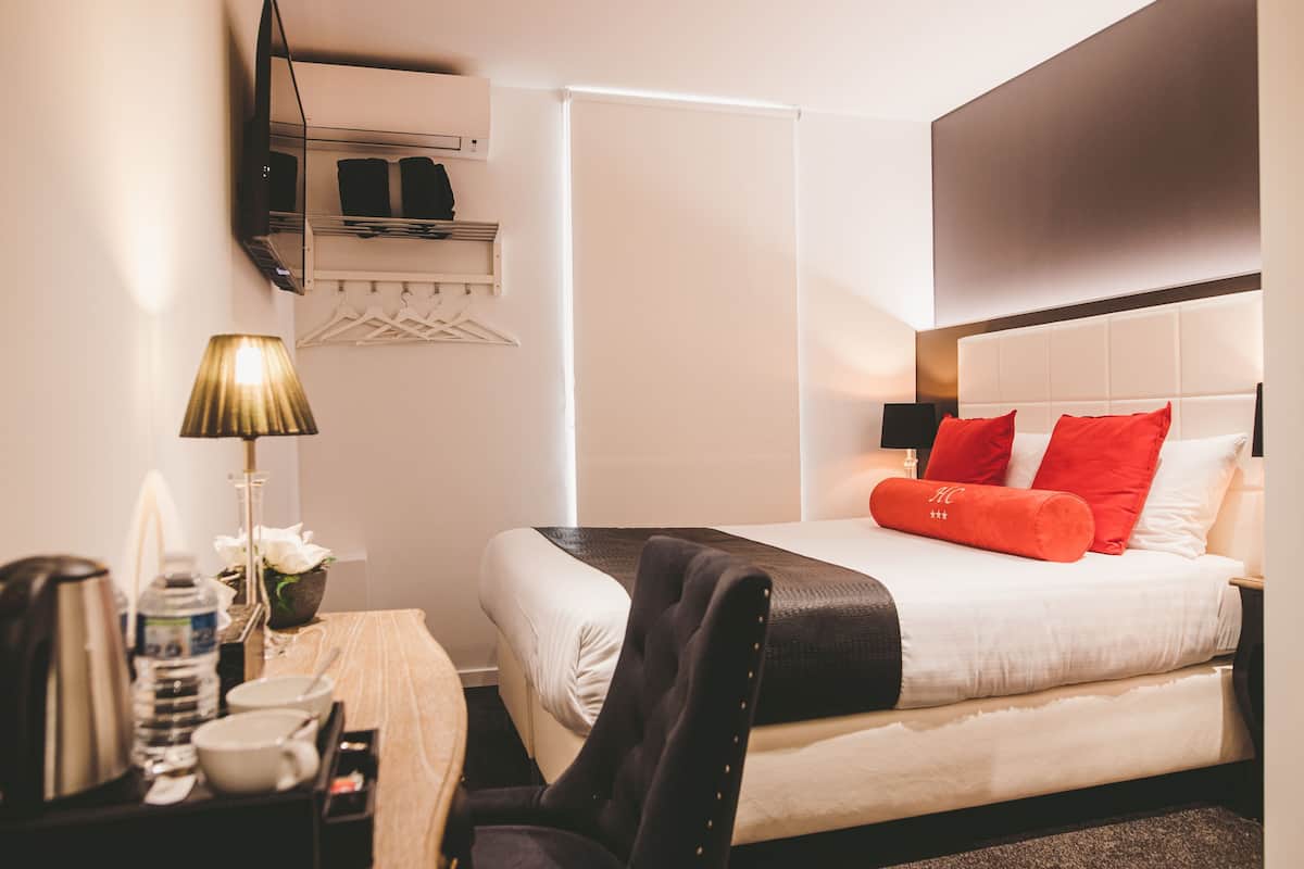 A hotel room with a bed, bedside table, lamp, and a TV mounted on the wall.
