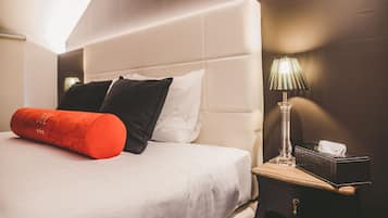 A neatly made bed with white and black pillows, a red accent pillow, and a bedside table with a lamp and a tissue box.