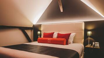 Habitación de hotel con techo alto, cama con ropa de cama roja y blanca, y mesita de noche con lámpara y teléfono.