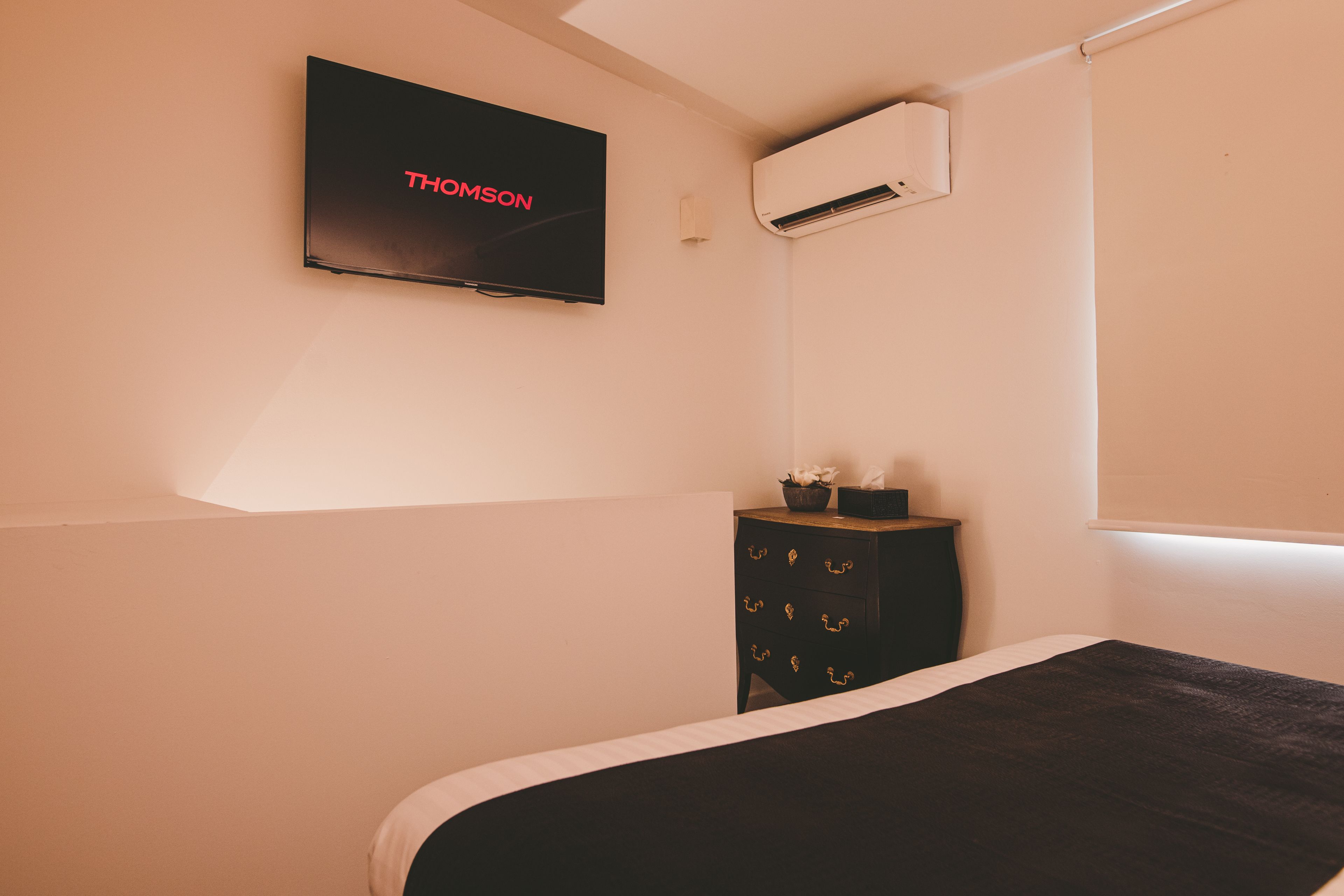 Une chambre à coucher comprenant un lit, une commode, un téléviseur fixé au mur et un appareil de climatisation.