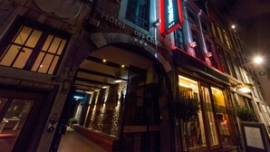 A hotel entrance with a stone facade, illuminated signage, and a visible entrance door. - Hôtel Hors Château (Liege)