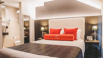 A hotel room with a large bed, a nightstand with a lamp, and a bathroom visible through an open door.