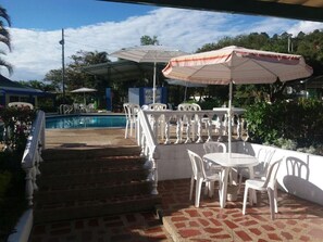 An outdoor patio area with white plastic chairs and tables, a pool, and a covered seating area with umbrellas. - Hotel Villa Paz (San Francisco)