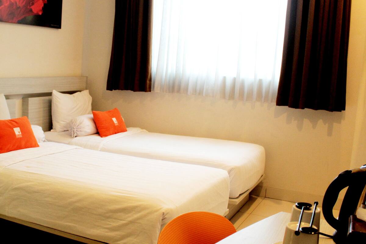 Ein Hotelzimmer mit zwei Einzelbetten, weißer Bettwäsche und orangefarbenen Kissen.
