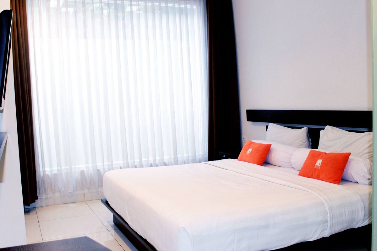 Ein Hotelzimmer mit einem großen Bett, weißer Bettwäsche und zwei orangenen Kissen.