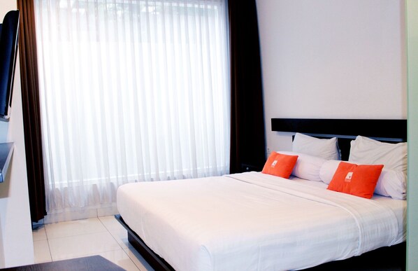 A hotel room with a large bed, white bedding, and two orange pillows. - V Hotel & Residence Bandung (Bandung)