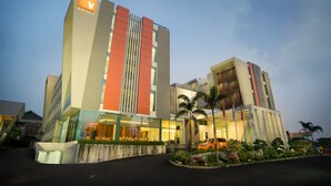 A modern hotel with a prominent 'V' logo, large windows, and a well-maintained garden area.