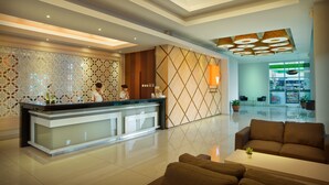 A modern hotel lobby with a reception desk, seating area, and a view of the restaurant in the background.