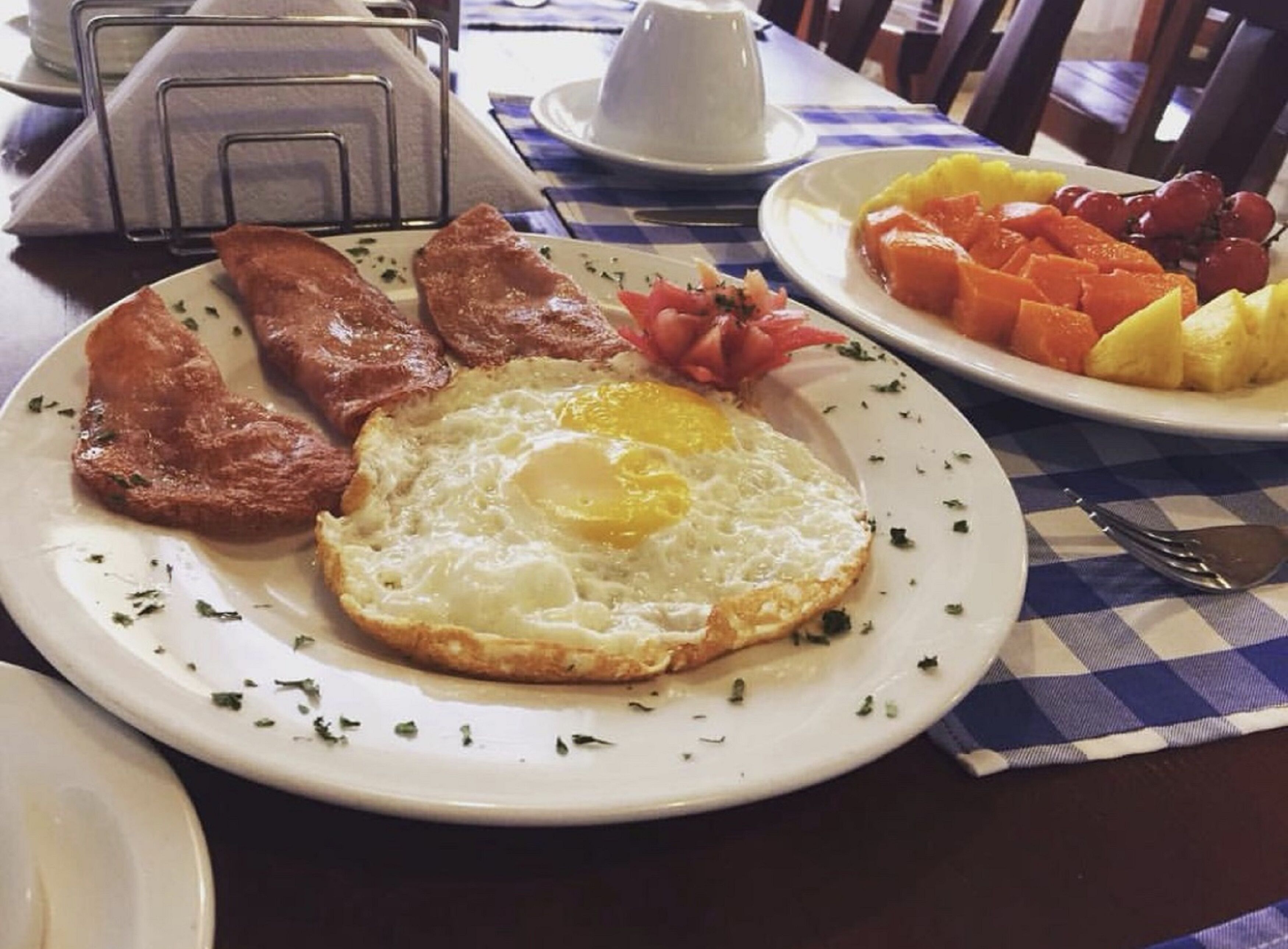 A breakfast plate with eggs, bacon, tomatoes, and fruit.