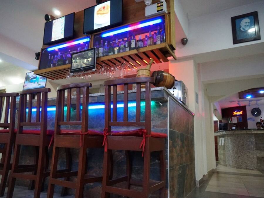 A bar area with wooden chairs, a counter with a television, and a neon sign.
