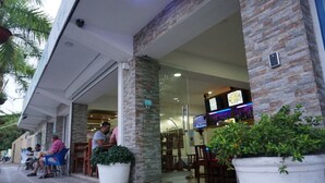 An outdoor seating area with chairs and tables, a potted plant, and a building entrance with glass doors. - Hotel Restaurant Hamilton (Boca Chica)