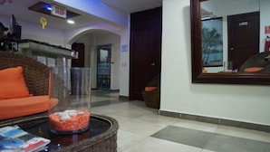 A lobby with a reception desk, a large mirror, a wicker chair, and a glass table with decorative items. - Hotel Restaurant Hamilton (Boca Chica)