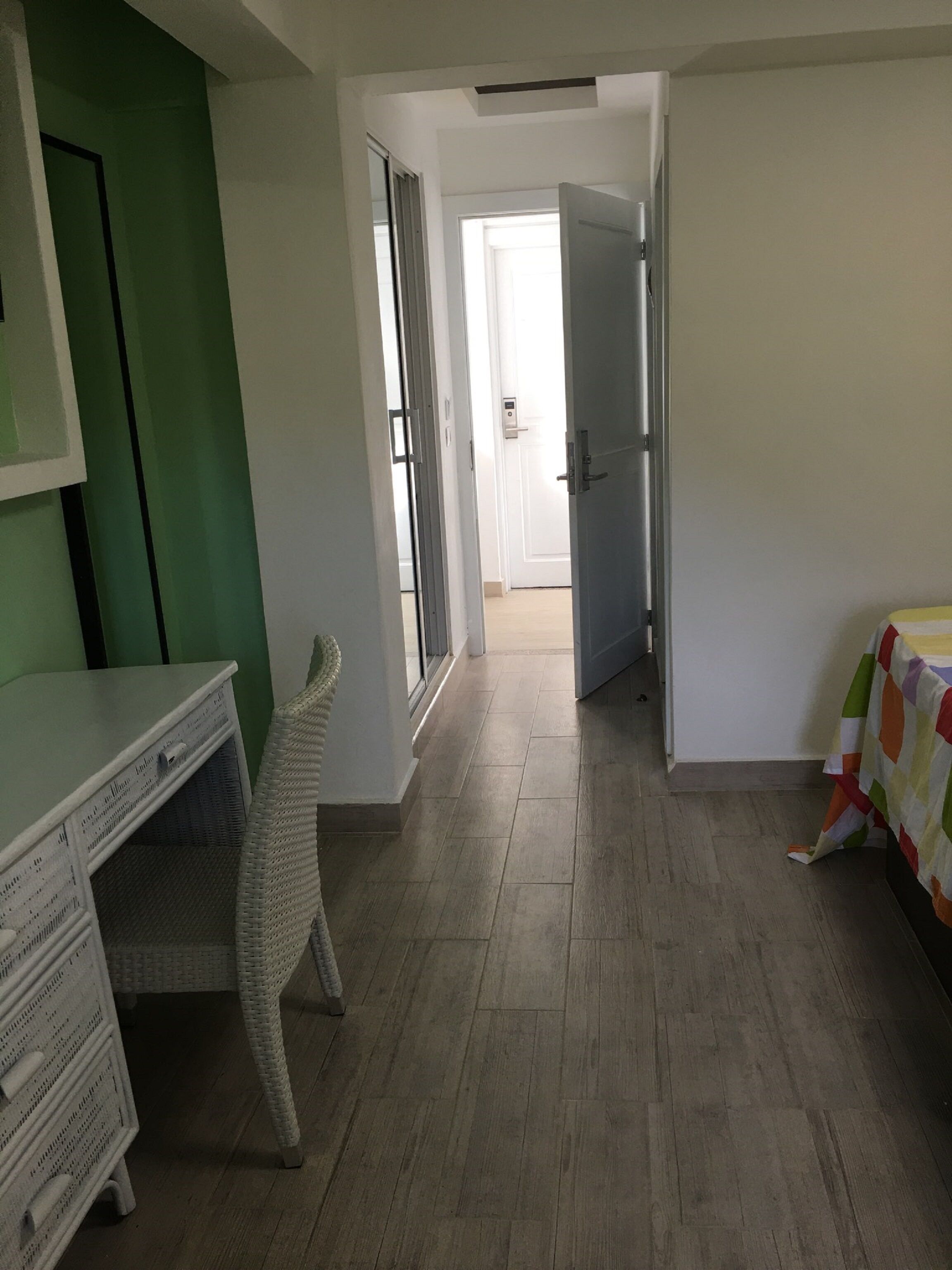 Een kamer met een bureau, een rieten stoel, een bed met een kleurrijk dekbed en een deur naar een andere kamer.
