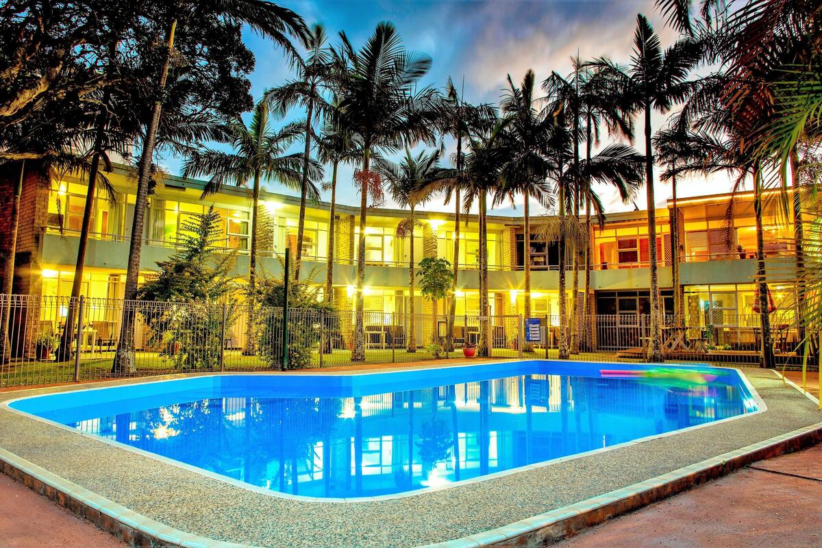 A hotel with a swimming pool surrounded by palm trees and a multi-story building with illuminated windows.