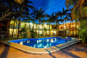 Une piscine entourée de palmiers et un bâtiment doté de nombreuses fenêtres et de balcons.