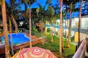 A pool area with a fenced deck, surrounded by palm trees and a colorful umbrella.