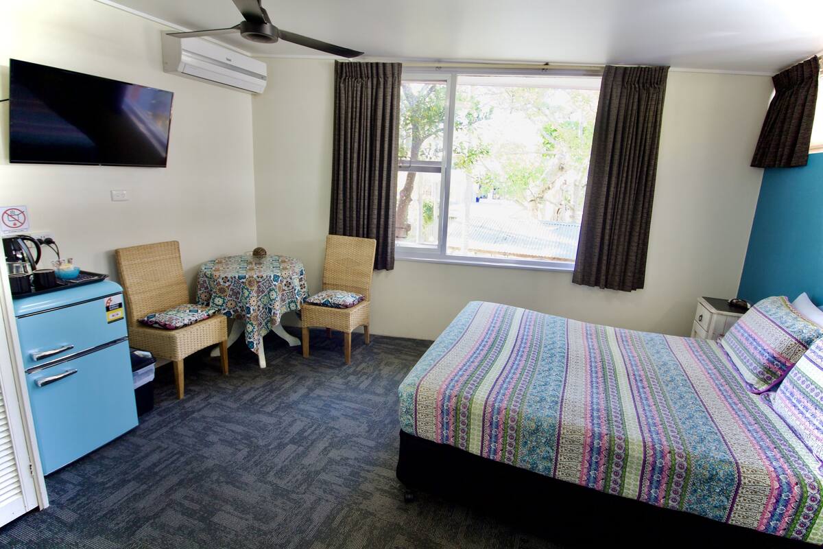 A room with a bed, a desk with a computer, a chair, and a window with curtains.