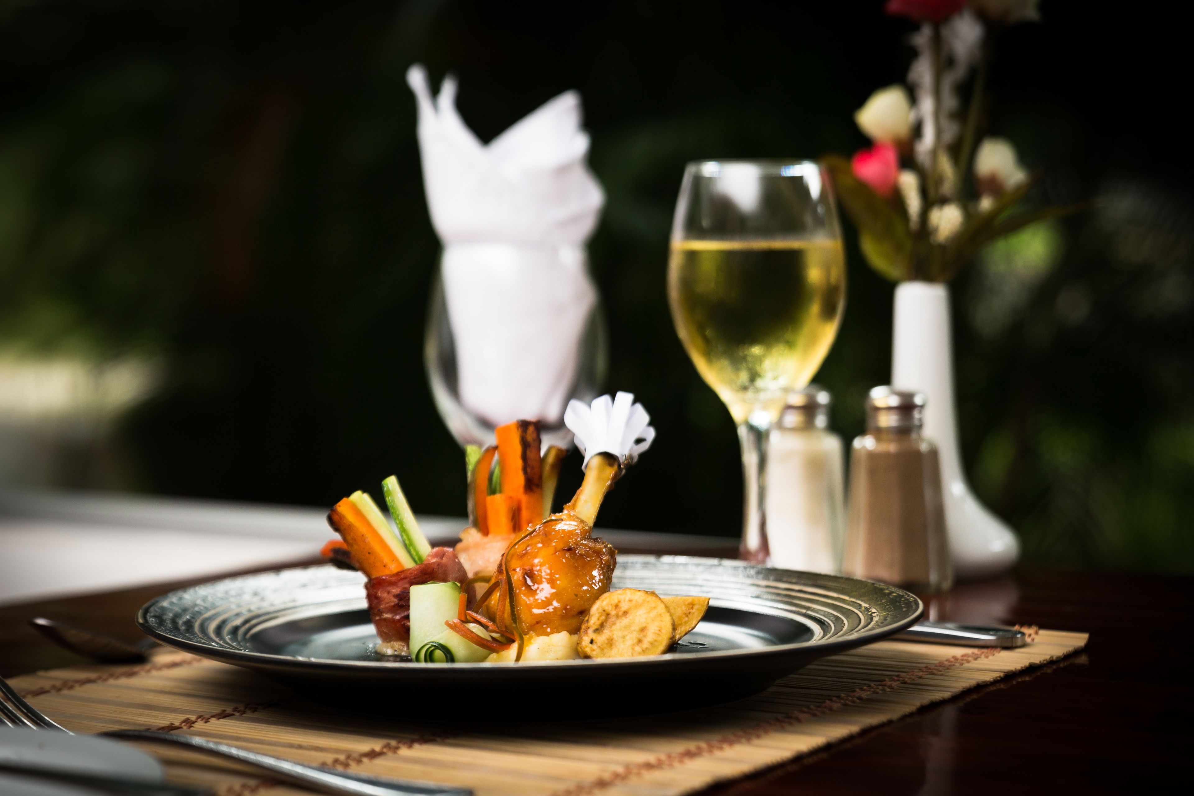 Ein Teller mit Essen, ein Glas Weißwein und Salz- und Pfefferstreuer auf einem Tisch.