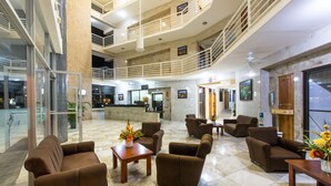 A spacious lobby with multiple seating areas, a reception desk, and a staircase leading to an upper level. - Hotel Arenas en Punta Leona (Tárcoles)