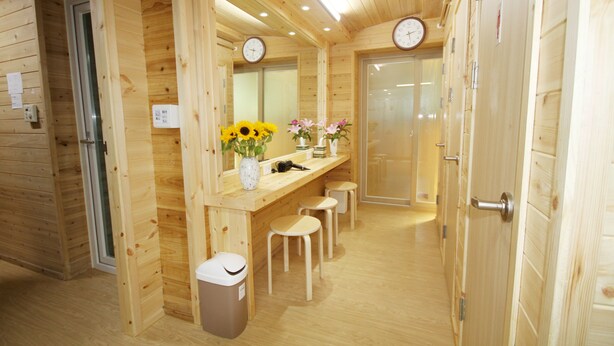 Un intérieur en bois avec un banc en bois, une poubelle et un miroir orné d’horloges.