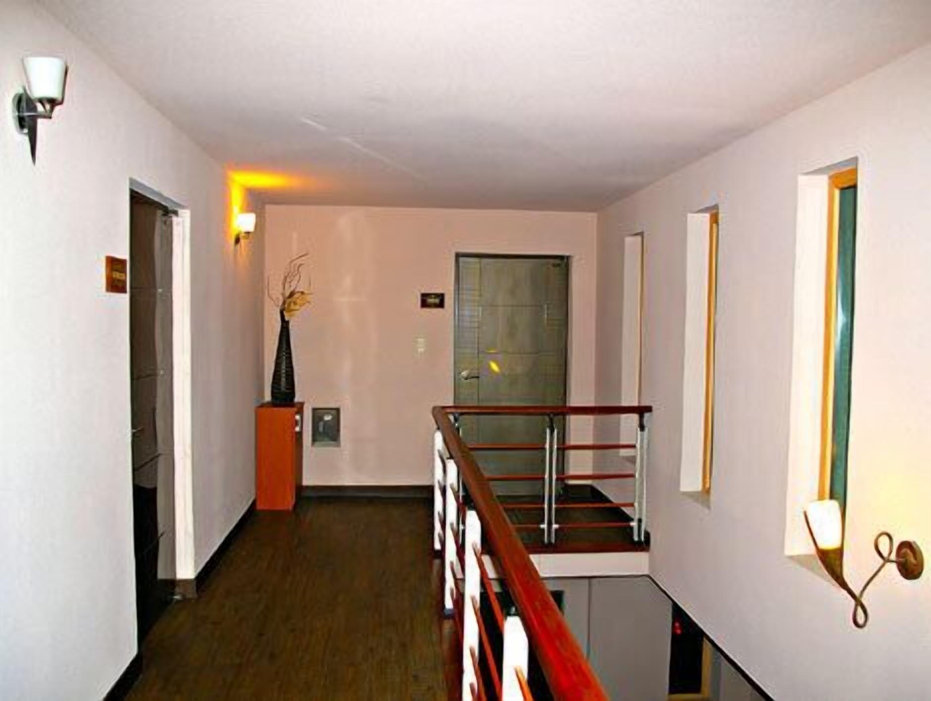 A modern hotel hallway with a wooden railing, a vase with branches, and a door at the end.