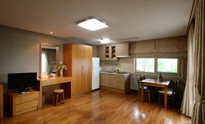 Eine kompakte Küche mit Holzausstattung, einem Essbereich mit Tisch und Stühlen, einem eingebauten Fernseher und einem Fenster mit Vorhängen.
