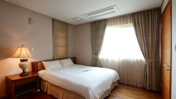 Una cama bien tendida en una habitación de hotel, con una mesita de noche, una lámpara y una ventana con cortinas.
