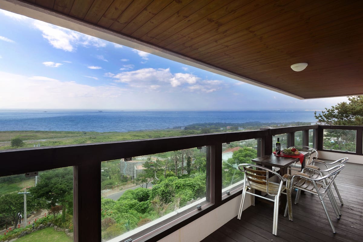 Un balcon avec une table et des chaises, offrant une vue panoramique sur l’océan et la végétation environnante.