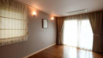 Ein Zimmer mit Holzboden, einem großen Fenster mit Vorhängen und zwei Wandleuchten.