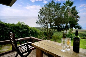 A wooden table with two wine glasses and a bottle of wine, overlooking a scenic view of the ocean and lush greenery.